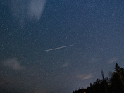Dark night sky at a rocky beach with a star trail