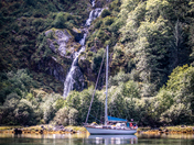 A beautiful sailboat in an anchorage in front of a waterfall in Khutze Inlet